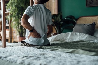 Man sitting on a bed holding his lower back because he is in pain