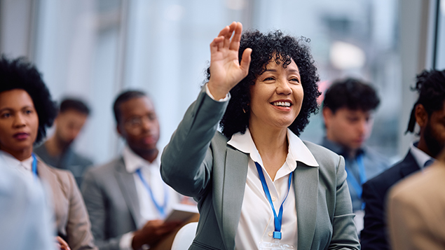 image of a woman seated with other audience members smiling and raising her hand