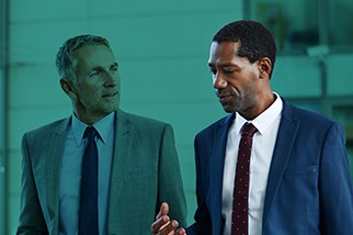 Two safety professional men in suits talking in front of a teal background
