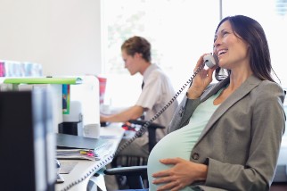 Pregnant worker smiling on the phone next to a colleague while sitting in a chair