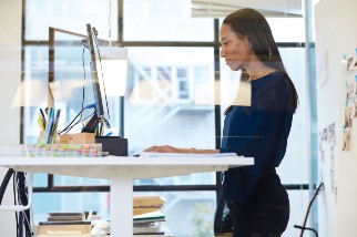 Safety professional woman using a sit stand workstation and looking at her computer in a brightly lit office