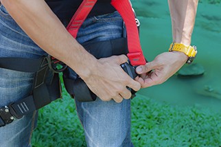 Closeup of man's hands putting on a fall protection harness in front of a teal background