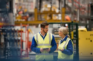 Two workers in high visibility vests and eye protection talking in a warehouse