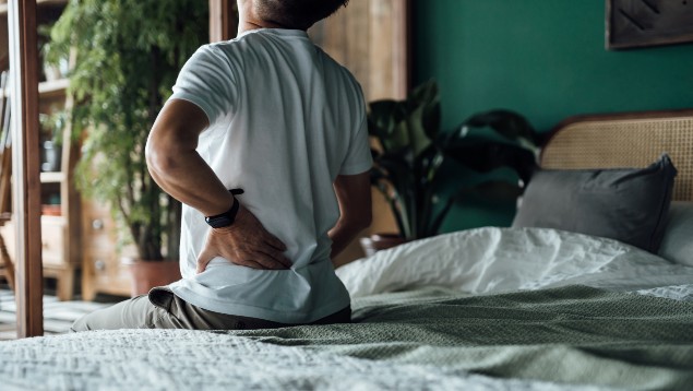 Man-sitting-on-a-bed-holding-his-lower-back-because-he-is-in-pain