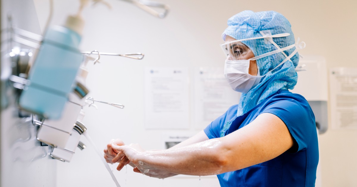 Female healthcare worker wearing blue scrubs and PPE washing her hands before a procedure