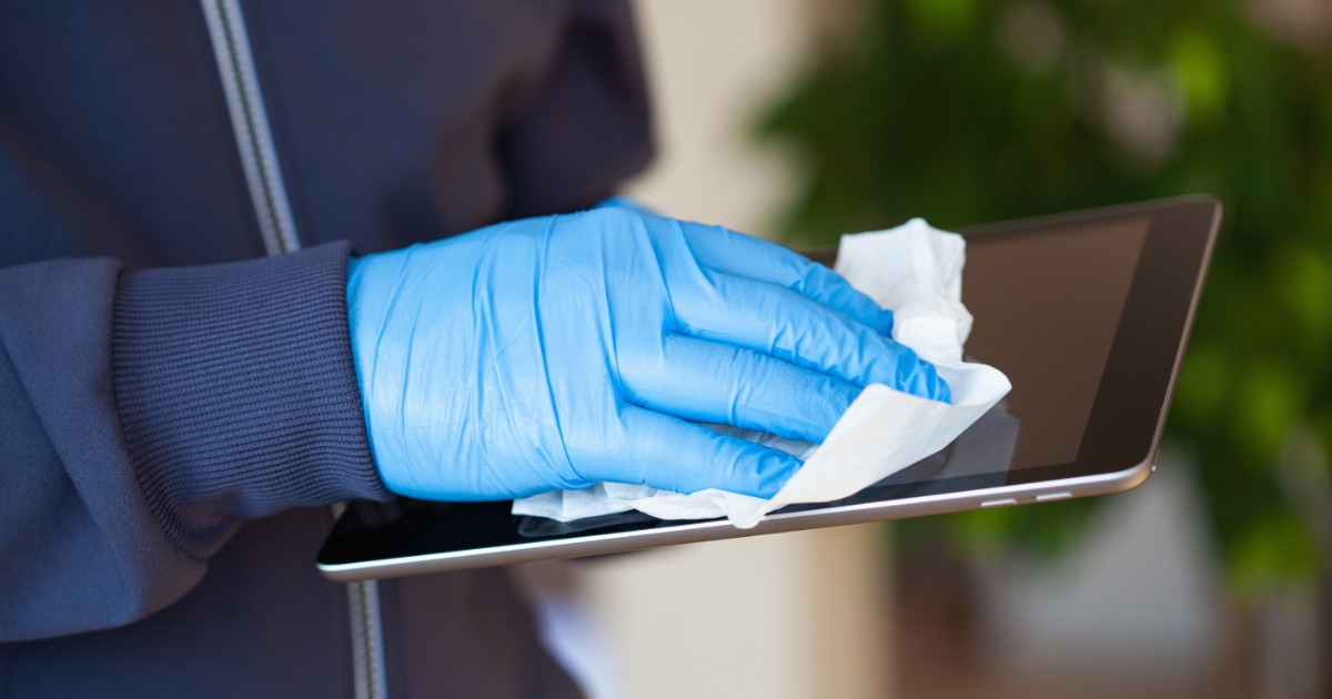 Person in a blue jacket and gloves cleaning a tablet