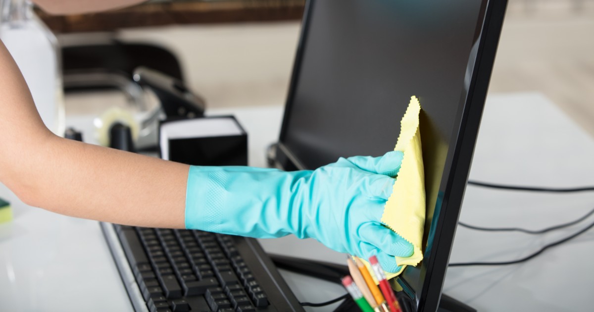 Womans hand in a blue glove wiping down an office computer monitor to prevent the spread of COVID-19