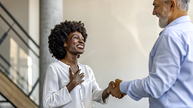 A smiling woman shakes hands with a man in an office hallway