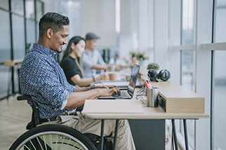 Asian Indian white collar male worker in wheelchair concentrating working in office beside his colleague