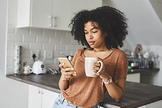 Shot of a young woman using a smartphone and having coffee in the kitchen at home